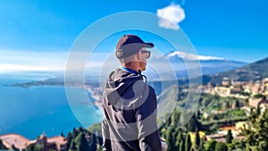 Toarmina - Tourist man with panoramic view on snow capped Mount Etna and the Mediterranean sea from Taormina, Sicily, Italy