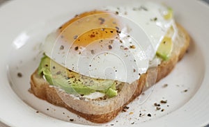 Toast with avocado on a white plate, made from whole grain bread, fried eggs