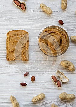 Toast, bowl of peanut butter, peanuts on a white wooden table, top view. From above, flat lay, overhead