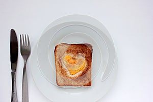 Toast bread with fried egg in a heart shaped hole on plate on white background. Creative Valentine\'s day