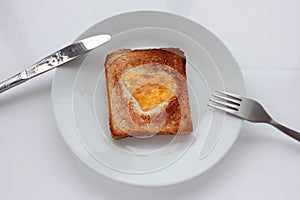 Toast bread with fried egg in a heart shaped hole on plate on white background. Creative Valentine\'s day