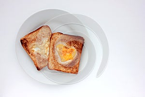 Toast bread with fried egg in a heart shaped hole on plate on white background. Creative Valentine\'s day