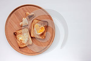 Toast bread with fried egg in a heart shaped hole on wooden board on white background.