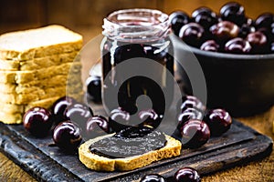 Toast with grape jam, on rustic wooden table. Jabuticaba, exotic Brazilian fruit, used in cooking, as a sweet
