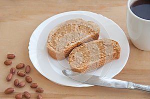 Toast with homemade peanut butter on a wooden table. A cup of coffee, knife and peanuts. Top view