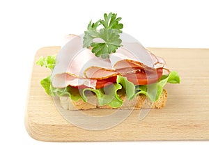 Toast,lettuce,tomato,cold cuts on cutting board on white