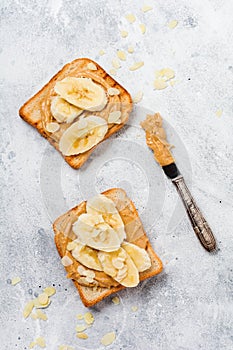 Toast with peanut butter, banana slices, honey and almond flakes on old gray concrete background.