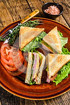 Toasted Club sandwiches with pork ham, cheese, tomatoes and lettuce on a plate. wooden background. Top view