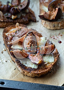 Toasted fig and prosciutto tartines on a parchment lined baking sheet.