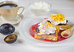 Breakfast of French bread with curd cream, plum jam and orange zest on a white table.