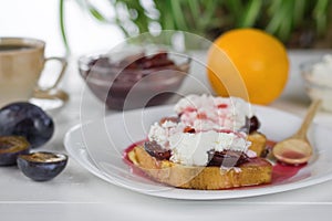 Toasted French bread with plum jam and a wooden spoon on a white plate.