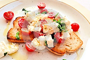 Italian bruschetta with fresh tomato, mozzarella, basil and olive oil, close up on a white plate