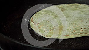 Toasted on one side pita bread turned over in the pan with an orange spatula, and corrected by a man`s hand