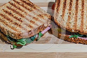 Toasted sandwiches with ham, cheese, tomatoes and salad on wooden cutting board
