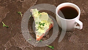 Toasts with avocado pate, fresh microgreen and cup of coffee on dark concrete background