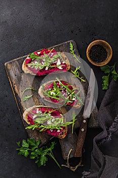 Toasts with beetroot hummus, feta cheese and arugula on cutting board