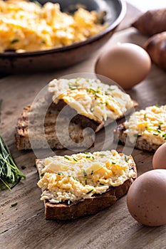 Toasts of bread with generous portion of scrambled eggs on top of it, sprinked with freshly chopped chives