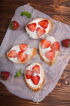 Toasts or bruschetta with strawberries on cream cheese on wooden background.