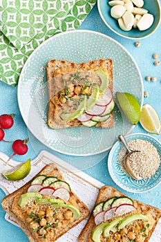 Toasts with chickpea hummus, avocado, fresh radish, cucumber, sesame seeds and flaxseed sprouts. Diet breakfast. Delicious and hea