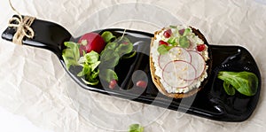 Toasts with cottage cheese and smashed avocado, radish, corn salad plant and pomegranate seeds on a serving bottle-plate.