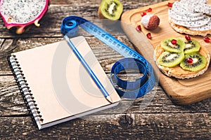 Toasts with fruit, measuring tape and empty notebook on wooden background. Slimming plan with fruits. Planning healthy diet