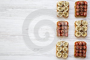 Toasts with peanut butter, fruits and chia seeds over white wooden background, top view. Healthy dieting.