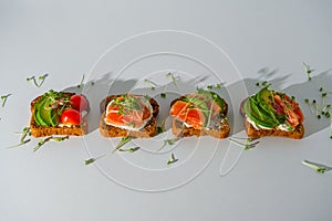 Toasts with salmon, trout, cherry tomatoes, avocado and microgreens on white background, healthy breakfast snack concept