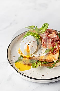 Toasts sandwich with poached egg, arugula, bacon and cream cheese on white plate marble background. Isolated, text space