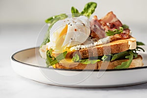 Toasts sandwich with poached egg, arugula, bacon and cream cheese on white plate marble background. Isolated, text space