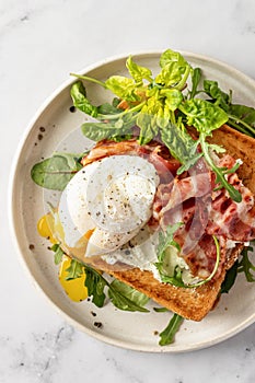 Toasts sandwich with poached egg, arugula, bacon and cream cheese on white plate marble background, top view, clole up