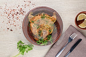 Tobacco chicken decorated with herbs on a clay plate on a white wooden table. Top view.