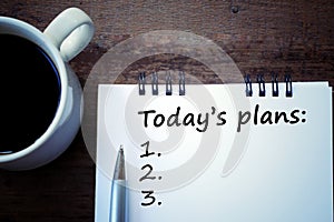 Today plans list with number written on notebook, a pen, and a white cup of morning coffee on a wooden table. Every organized