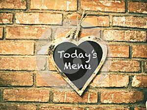 Today`s menu on heart shape chalkboard on concrete wall, restaur