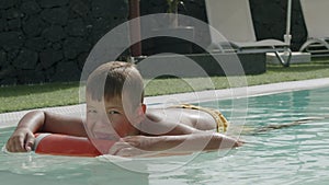 Today he is too lazy to swim. Relaxed boy floating on safety ring in the pool