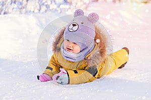 Toddler 12-17 months old in yellow winter clothes slipped and fell on ice while walking in a winter park