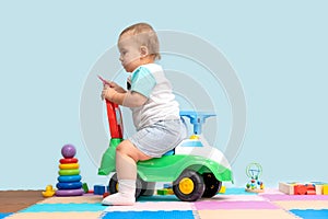 Toddler 15-20 months sitting on a children`s toy car backwards in the playroom