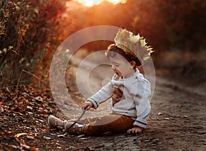 Toddler in the autumn leaves. Beautiful little child on an autumn walk looks at the falling foliage. Baby boy sitting on