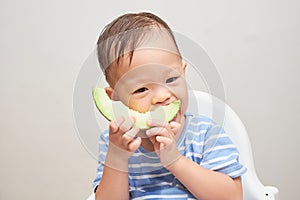 Toddler baby boy child eating melon, Little kid sitting in high chair eating fruit, Self feeding