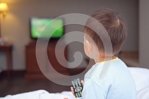 toddler baby boy child sitting in bed holding the tv remote control and watching television