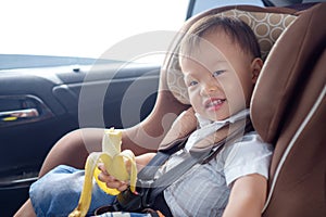 Toddler baby boy child sitting in safety carseat holding & enjoy eating banana photo