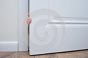 Toddler baby boy holds the edge of the open door with his hand. Close-up child hand at the door jamb