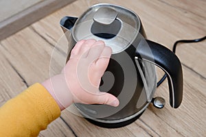 Toddler baby boy holds a hot kettle with boiling water. Child safety issues in the home room, little kid