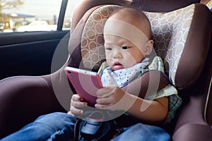 Toddler baby boy sitting in car seat and watching a video from smart phone