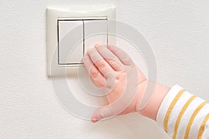 Toddler baby boy turns the light on and off with an electric switch. Close-up of a child hand at a double light switch