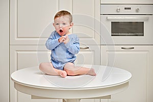 Toddler baby climbed on the kitchen white table. A child in danger clim