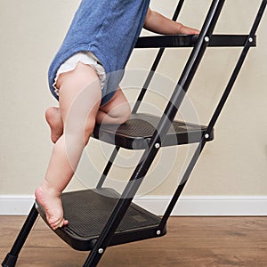 Toddler baby climbs on the steps ladder. Child boy climbs up the stairs