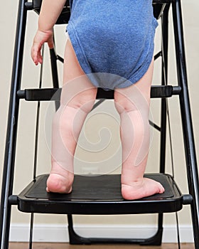 Toddler baby climbs on the steps ladder. Child boy climbs up the stairs