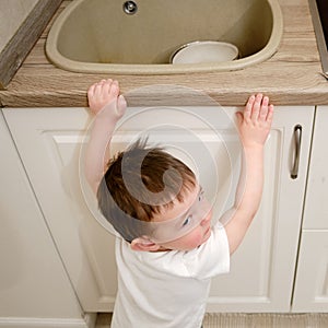 Toddler baby climbs to the sink in the home kitchen. A small child touc