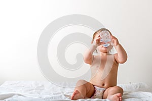 Toddler baby drink water from blue plastic bottle. Sitting on white background. Copy space