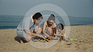 toddler baby girl playing sand toy with her father and mother. happy family on sea beach